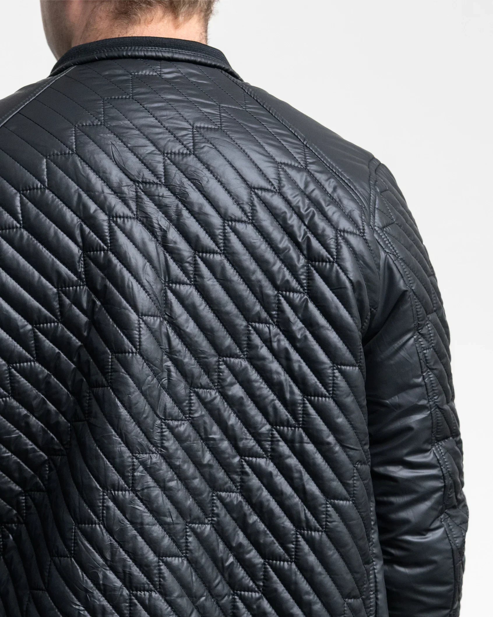 Black quilted jacket back view with diamond stitching and ribbed hem cuffs.
