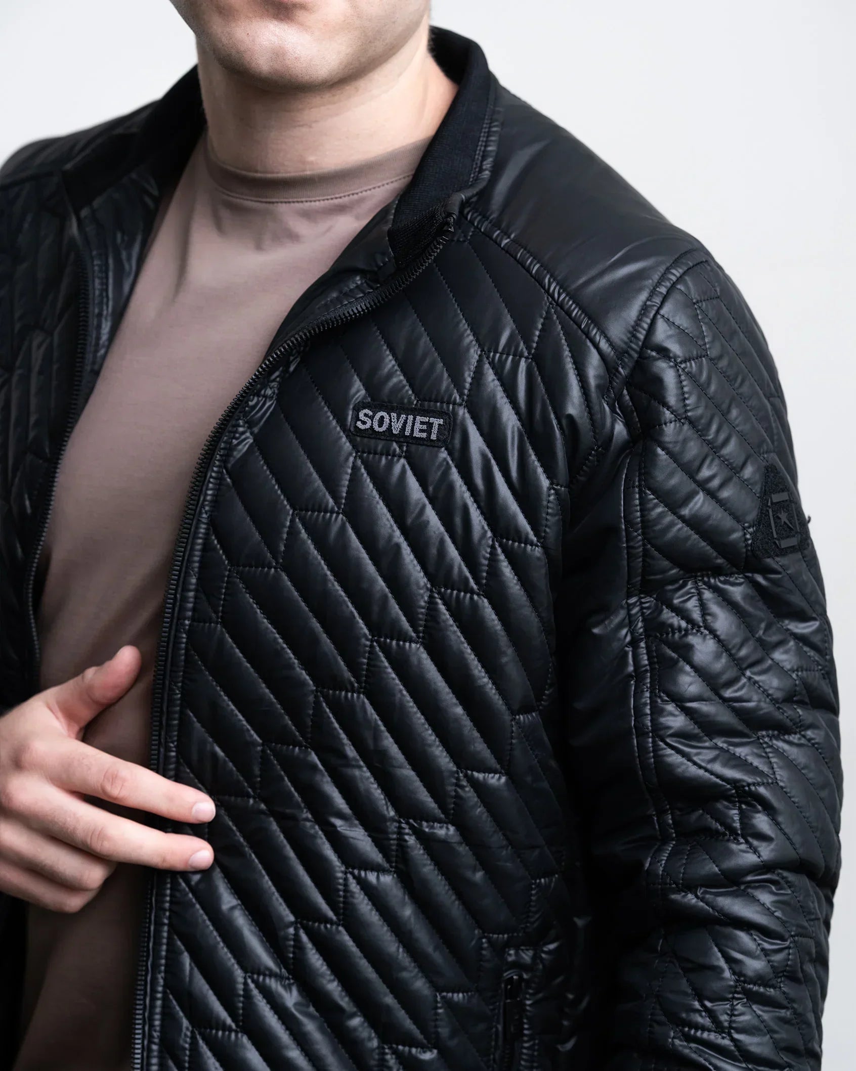 Black quilted jacket with full-zip, stand collar, and chest logo patch.