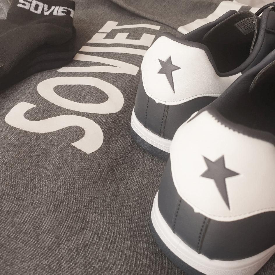 Black and white sneakers with star detail, black socks, and grey sweatshirt with bold text