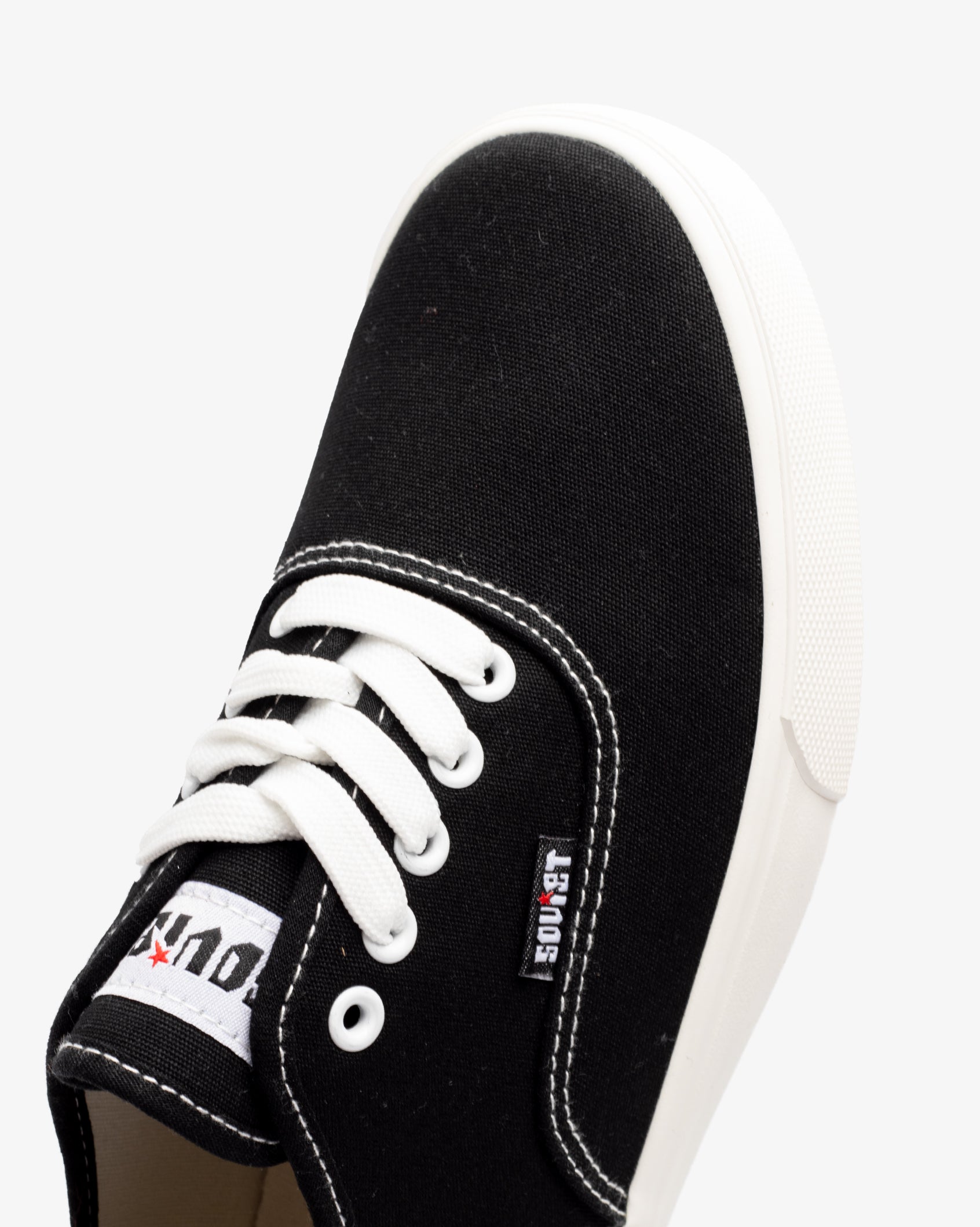 Men's low-cut canvas sneakers, black; toe close-up with white laces and eyelets.