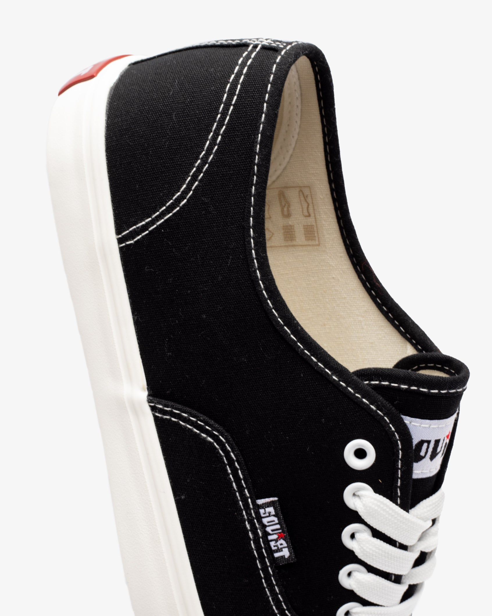Men's low-cut canvas sneakers, black; heel and side panel close-up with white laces.